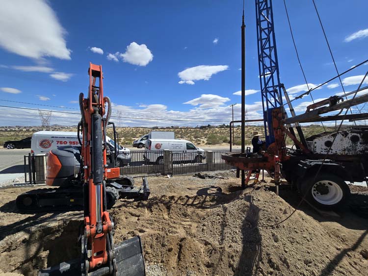 Excavator and drilling rig operating during a septic seepage pit installation in Victorville